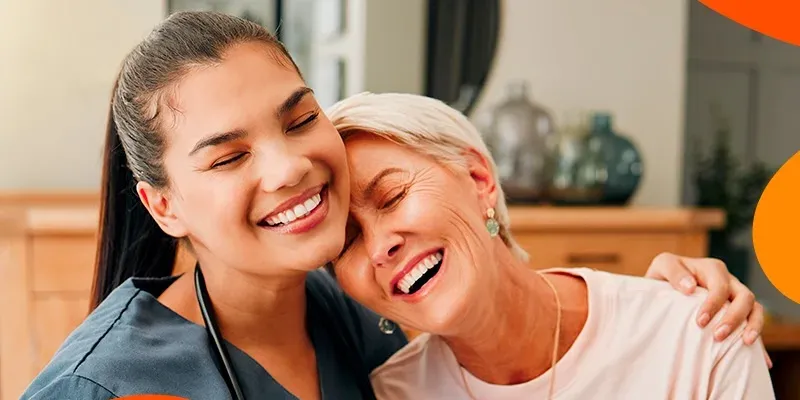 Enfermeira abraçada a uma senhora sorridente